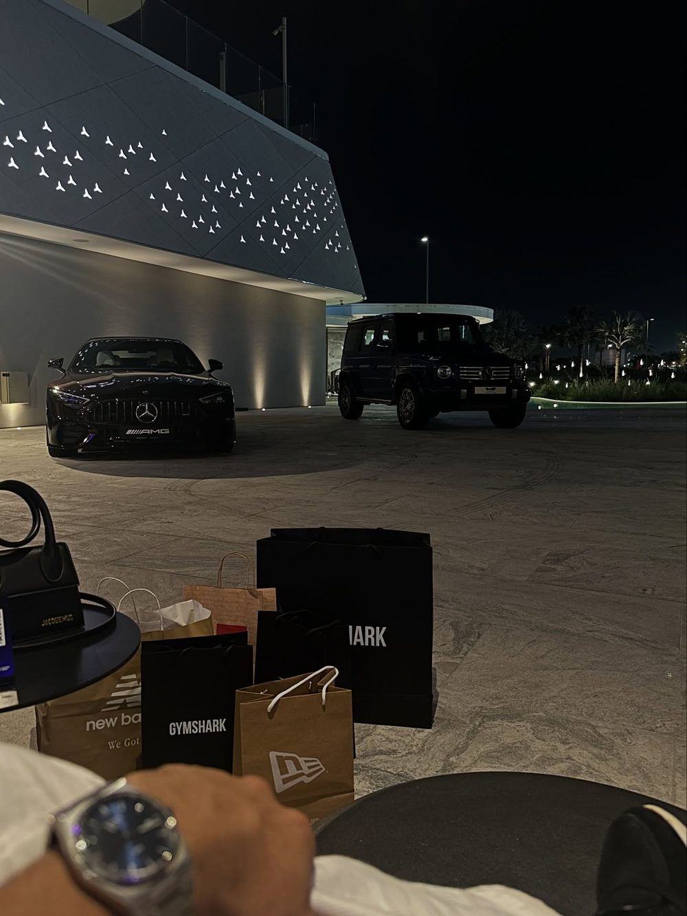 Luxury cars parked outside a building at night with shopping bags