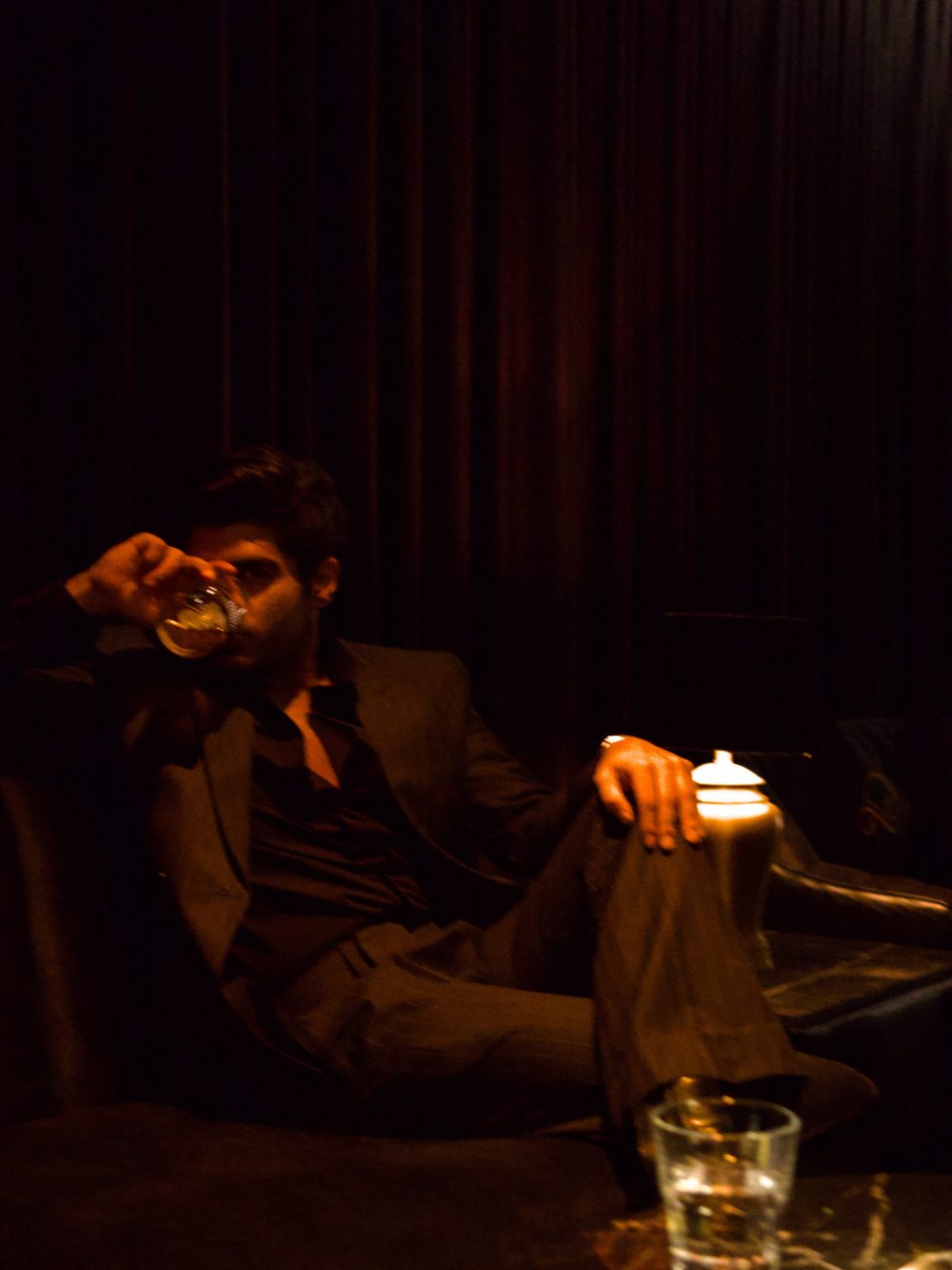 Man in a dark suit relaxing on a couch in a dim lounge